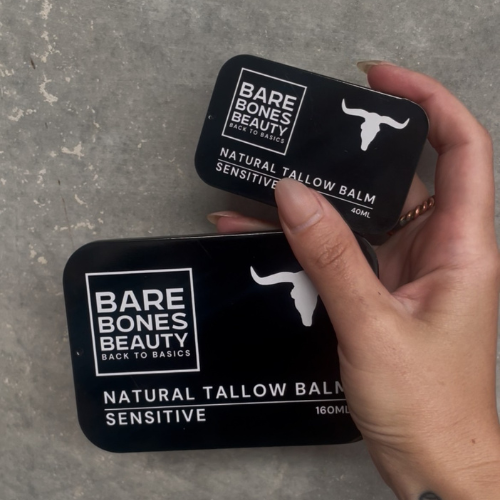 
                  
                    A hand with long nails holds two black tins labeled "Bare Bones Beauty Australia Sensitive Tallow Balm" in 40ml and 160mL, featuring Organic Tallow for deep hydration, against a gray textured background.
                  
                