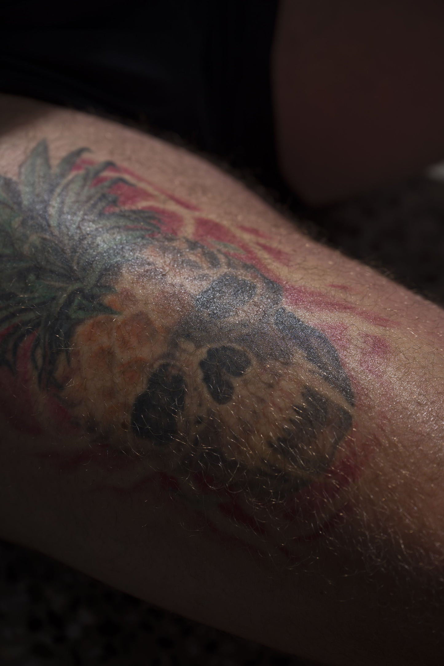 A pineapple skull tattoo on a hairy arm under shaded light—ideal to showcase skin recovery with Bare Bones Beauty Australia's Tattoo Balm.