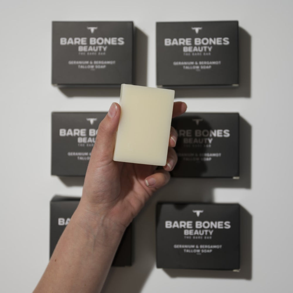 
                  
                    A hand holds The BARE bar – Tallow Soap from Bare Bones Beauty Australia before six black boxes on a white surface, showcasing the product's moisturizing cleanse.
                  
                