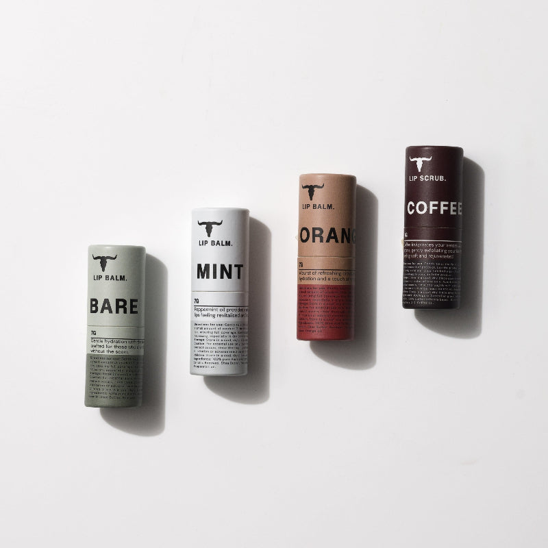 Four cylindrical lip care products in different colors labeled: BARE (green), MINT (white), ORANGE (orange), and COFFEE (brown) are neatly arranged side by side on a white background.