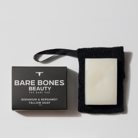 A rectangular white bar of The BARE Bar – Tallow Soap by Bare Bones Beauty Australia sits on a black exfoliating bag next to its black box packaging.