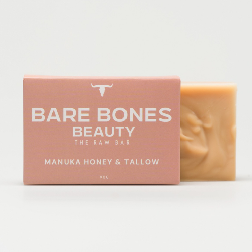 A pink box labeled "Bare Bones Beauty Australia: The RAW Bar – Tallow Soap" stands beside an unwrapped beige soap with grass-fed beef tallow and Manuka Honey, set against a plain white background.