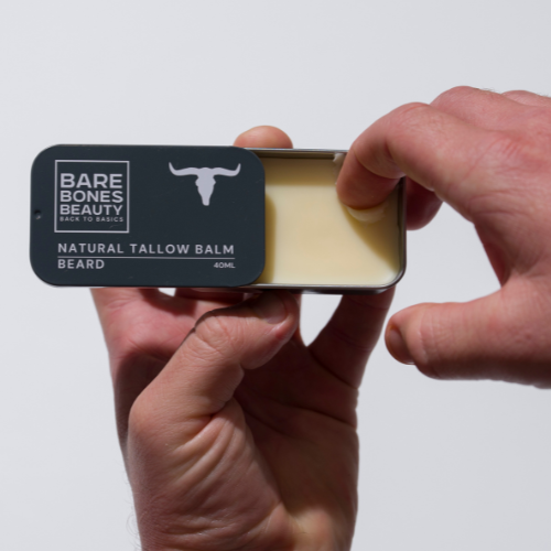 A hand slides open a Bare Bones Beauty Australia Beard Balm - Vintage Tin, revealing a creamy natural hair moisturizer inside, set against a plain white background.