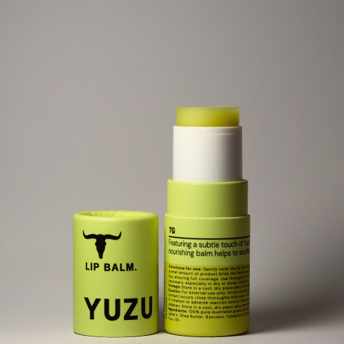 
                  
                    A yellow tube of Bare Bones Beauty Australia Yuzu Balm stands upright with the cap off. The label shows a bull logo, black "LIP BALM. YUZU" text, and instructions. Made with grass-fed beef tallow for deep hydration.
                  
                